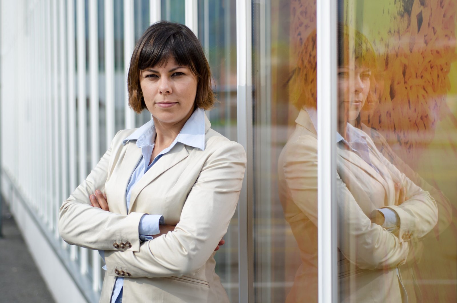 businesswoman in a suit standing in front of a glass window with crossed arms